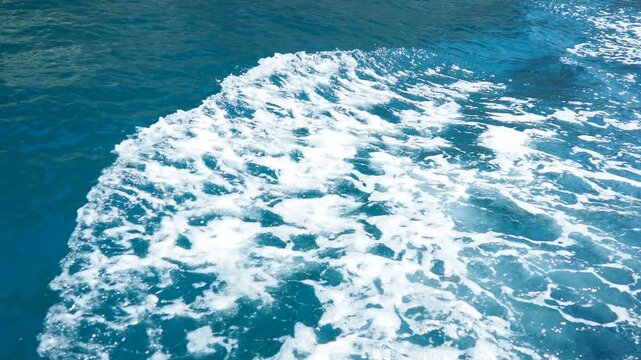 Yacht waves moving on azure Adriatic Mediterranean Sea. Blue water surface, foam bubbles. Travel, boat trips, summer holidays, tourism Montenegro, Budva region, bay of caves, shark bay near Petrovac.