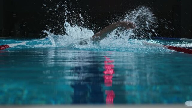 Slowmo of determined male athlete swimming towards camera in indoor pool while training for swimming competition alone