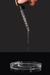 Serum drops fall from a pipette on a petri dish against  black background