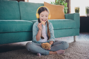 Full length portrait of cute little girl headphones eat cookie wear shirt loft interior modern flat...
