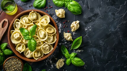 Fototapeta premium Fresh tortellini pasta in a wooden bowl with basil leaves on a dark slate background. Culinary photography depicting healthy Italian cuisine. 