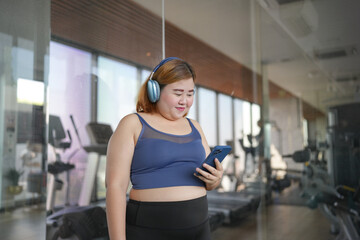 Fototapeta premium Obese asian woman Enjoy listening to music. Fat Female with headphones smart phone after workout at Gym