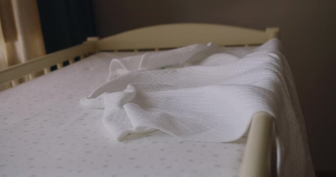 Modern empty wooden crib with mattress, cotton sheet and blanket in nursery room. Preparing baby bed for newborn comfort sleep. Wooden crib with mattress, cotton sheet and blanket in nursery room.