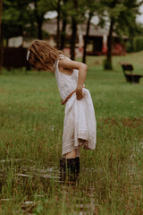 Dziewczynka w kaloszach skacze w kałuży w białej sukience © katarzyna