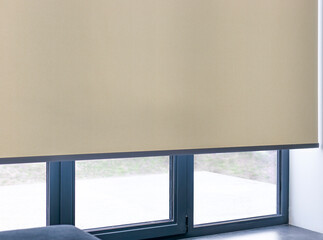 Roller blinds on full height window. Automated smart curtains indoors. A beige electric roller shade covers a large window, providing a minimalist aesthetic while filtering natural light.  