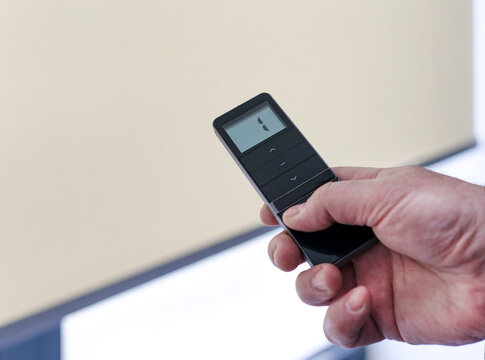 Remote control for window blinds. Man holds in his hand black remote control panel with display and operate motorized roller shades. Radio control electric blinds close-up.