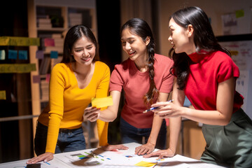Fototapeta premium Three young asian businesswomen are working late in the office, brainstorming ideas for their next project