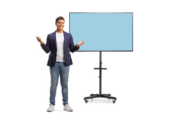 Full length portrait of a happy young man in jeans and suit presenting in front of tv screen on a...