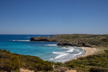 Obraz premium Tortuga beach, a pristine beach with golden sand and crystal-clear turquoise waters. Surrounded by green hills and rocks, the scene conveys tranquility and natural beauty. Menorca, Spain