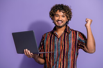 Photo of satisfied nice man with wavy hairdo dressed print shirt hold laptop win lottery say yeah isolated on purple color background