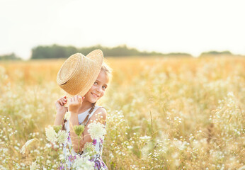Naughty girl with pigtails and a straw hat in a blooming summer field.