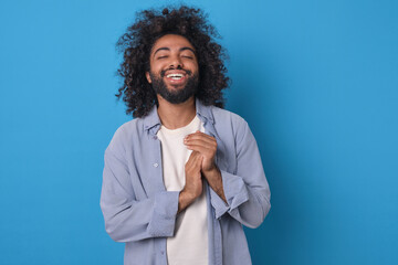 Young man with curly hair and a beaming smile stands against a vibrant blue backdrop, radiating joy...