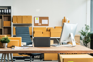 A wooden desk in an SME office, with a laptop, desktop computer, and a parcel cardboard box. The workspace is organized for efficient management, logistics, and order processing.