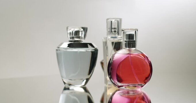 A collection of elegant perfume bottles displayed on a mirror surface creating captivating reflections. The assorted shapes and colors of the bottles evoke a sense of luxury and sophistication.