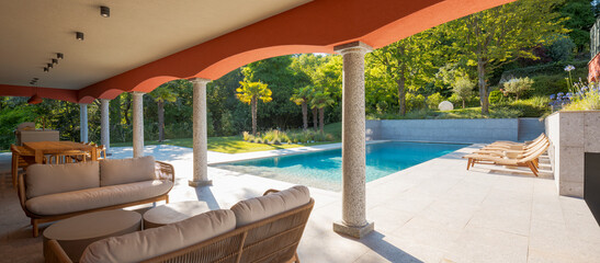 View of a beautiful swimming pool of a private property in broad daylight. A lounge under arches...