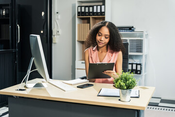 An African American woman with an afro works at a wooden desk in an office, focusing on business...
