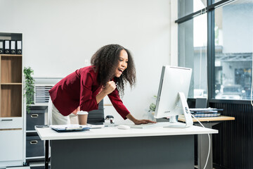 An African American woman with an afro works at a wooden desk in an office, focusing on business...