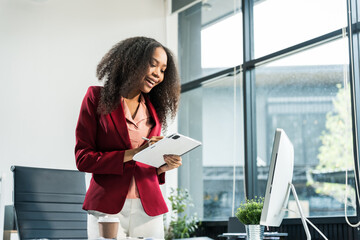 An African American woman with an afro works at a wooden desk in an office, focusing on business...