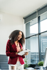 An African American woman with an afro works at a wooden desk in an office, focusing on business finance for startup. She manages market research, scalability, and interacts with angel investors.