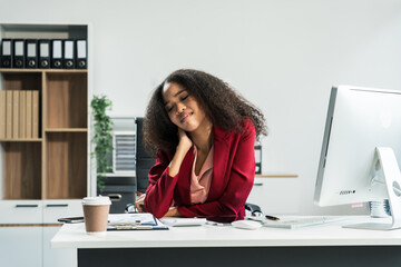 A hardworking African American woman with an afro sits tired at a wooden desk, suffering from...