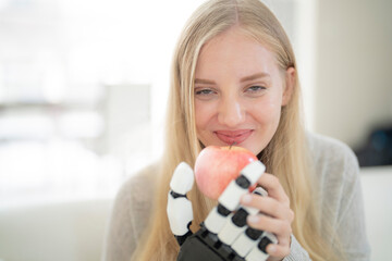 A young woman is using a robotic prosthetic arm attached to her body. She controls her hand to pick...
