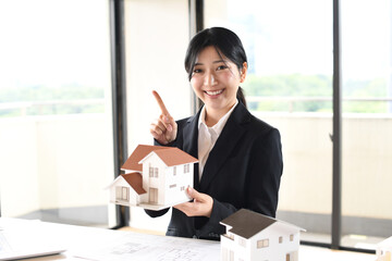 住宅模型を持ち人差し指を振るう女性会社員