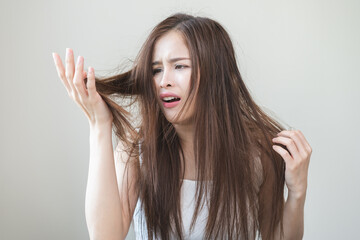 Fototapeta premium Damaged Hair, frustrated asian young woman, girl hand in holding splitting ends, messy unbrushed dry hair with face shock, long disheveled hair, health care of beauty. Portrait isolated on background.