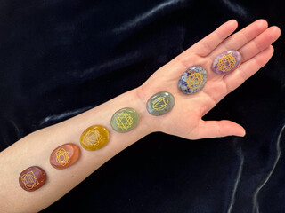 Human Arm Displaying Seven Chakra Stones on Dark Background.