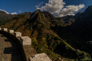  Scenic mountain landscape with deep green gorge, traditional village, and dramatic peaks under a...