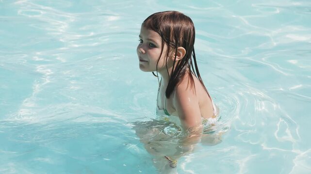 A girl happily splashes around in the pool, enjoying a summer day. Perfect for advertising related to children's activities, family events, and summer products.