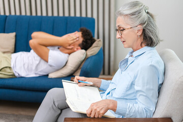 Obraz premium Psychotherapist taking notes while patient lying on couch is covering face