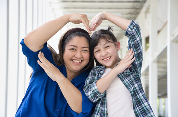 Lovely family of Asian mother and daughter. Happy Asian family with middle-aged mom and young female primary school girl posing big heart hand gesture, concept of Happy Family Day and Togetherness