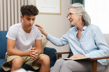 Psychologist comforting sad teenage boy during therapy session in psychology office