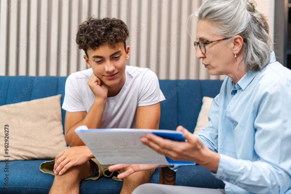 Wall mural senior female psychologist showing treatment plan to teenage boy during therapy session