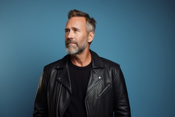 Obraz premium Portrait of a satisfied man in his 40s sporting a classic leather jacket isolated in pastel blue background