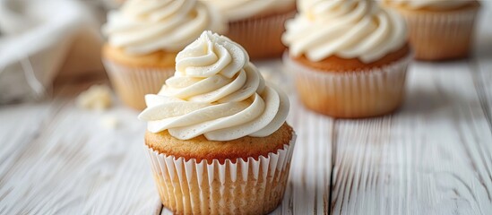 Vanilla cupcakes with cream cheese frosting displayed on a white wooden surface with selective focus and copy space image