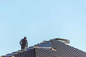 Workers installing metal tile on the roof while roofing house in construction site