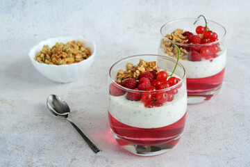a glass of yogurt with chia seeds, jelly and berries and a spoon next to it 