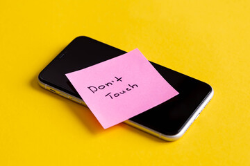 Inscription Don't touch, on a paper reminder on smartphone on a yellow background, digital detox,...