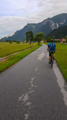 Rear view of man cycling along the Alpe Adria trail in Friuli-Venezia Giulia, Italy, Europe. Scenic mountain road, surrounded by nature beauty and remote village in Northern Italy