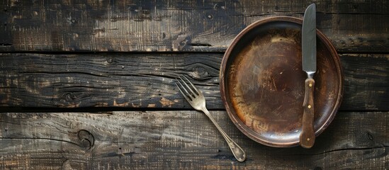 Wooden background with an empty plate an aged fork and knife creating a rustic tableau with copy space image