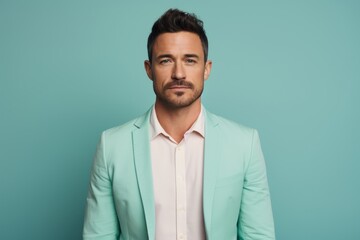 Portrait of a blissful man in his 30s dressed in a stylish blazer isolated in pastel teal background