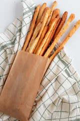 Deliciously crispy and savory breadsticks artfully wrapped in paper on a checkered cloth surface. Tasty grissini