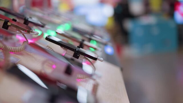 A close-up view of a row of smartphones on display in a store, each connected with a security cable and illuminated by colorful lights, with blur view of people at the background