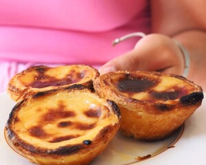 A close-up of an unidentifiable  woman holding a plate with three traditional Portuguese pastéis de nata or egg tarts. The delicious custard tarts are golden and crispy