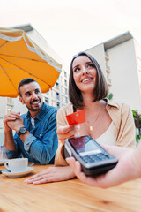 Vertical couple paying the bill of the coffee shop using a contactless creditcard payment. Young...