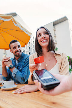 Vertical couple paying the bill of the coffee shop using a contactless creditcard payment. Young adult customer woman doing a purchase on a restaurant to the cashier with a debit card. People spending