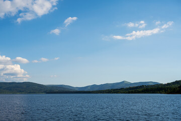 White puffy clouds and blue sky above Vlasina Lake. White cumulus clouds and a blue sky with sun rays. Beautiful semi-artificial lake in Southeast Serbia. 