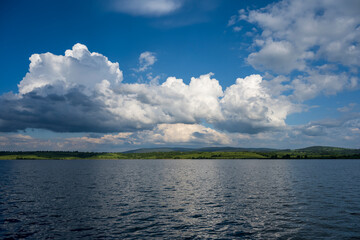 White puffy clouds and blue sky above Vlasina Lake. White cumulus clouds and a blue sky with sun rays. Beautiful semi-artificial lake in Southeast Serbia. 