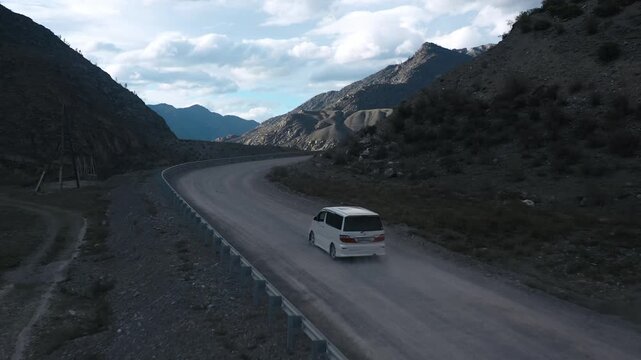 White automobile transportation riding on highway of alpine valley with river sunny landscape drone shot. Auto travel trip on path surrounded natural sunlight highland cliff rock geology formation